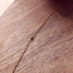 May include: A delicate gold-toned chain necklace featuring a series of small, evenly spaced round metal beads integrated directly into the link structure. The chain consists of thin, interlocking circular links that create a continuous, refined appearance.
