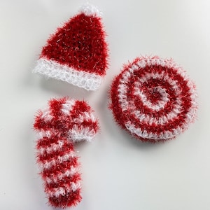 May include: Three handmade Christmas decorations are shown. They include a red and white Santa hat, a candy cane, and a circular ornament with red and white stripes. All are made of a fuzzy material.