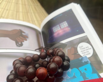 May include: A close-up of a brown wooden beaded bracelet with a blue and white book with the text "Yeah! These are much better than my old ones!" in the background.