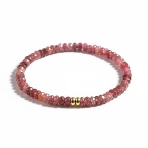 May include: A beaded bracelet featuring small, faceted pink gemstones. The bracelet is strung together with a gold-colored accent. The gemstones vary in shades of pink and red.