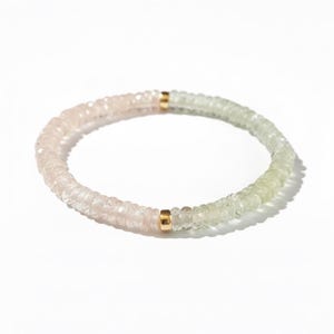 Puede incluir: Una pulsera de cuentas con pequeñas cuentas facetadas y translúcidas en un degradado de rosa pálido a verde claro. El hilo circular está acentuado por dos pequeños espaciadores cilíndricos de metal dorado pulido en los lados opuestos.