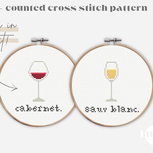Puede incluir: Dos patrones de bordado de punto de cruz en aros de bordado. El aro de la izquierda muestra una copa de vino tinto con el texto "cabernet". El aro de la derecha muestra una copa de vino blanco con el texto "sauv blanc."