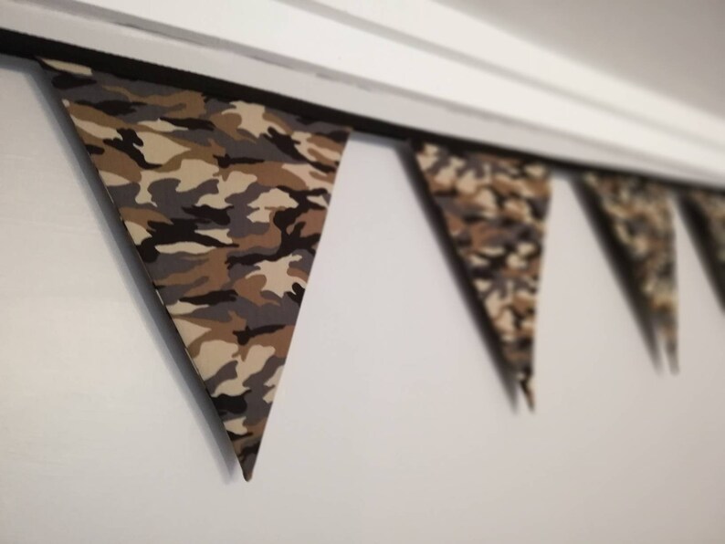 Puede incluir: Una guirnalda de tela con estampado de camuflaje con banderas triangulares. La guirnalda est&aacute; colgada del techo.