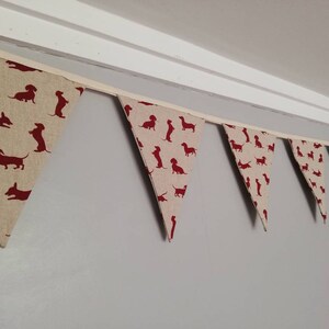 May include: A bunting with a string of triangular flags featuring a repeating pattern of red dachshund silhouettes on a beige background.