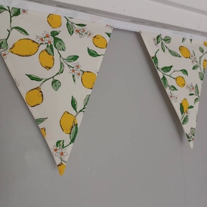 May include: A white bunting with a lemon print. The bunting is made of fabric and has a yellow and green lemon design. The bunting is hanging from a white ceiling.