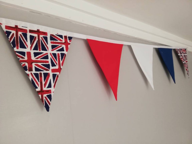 May include: A bunting with red, white and blue triangular flags. The flags are made of fabric and have a Union Jack pattern.