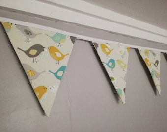 May include: A bunting with a white background and a repeating pattern of colourful birds. The birds are yellow, blue, and grey. The bunting is made of fabric and is strung together with white string.