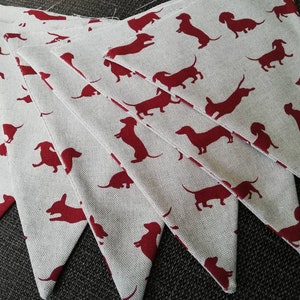 May include: A set of seven white fabric pennants with red dachshund silhouettes. The pennants are sewn together to create a garland.