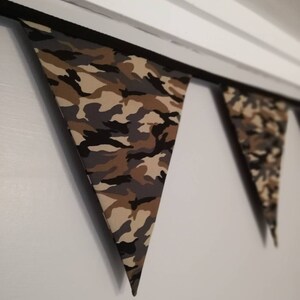 Puede incluir: Una guirnalda de tela con estampado de camuflaje con banderas triangulares que cuelgan de una cuerda negra.