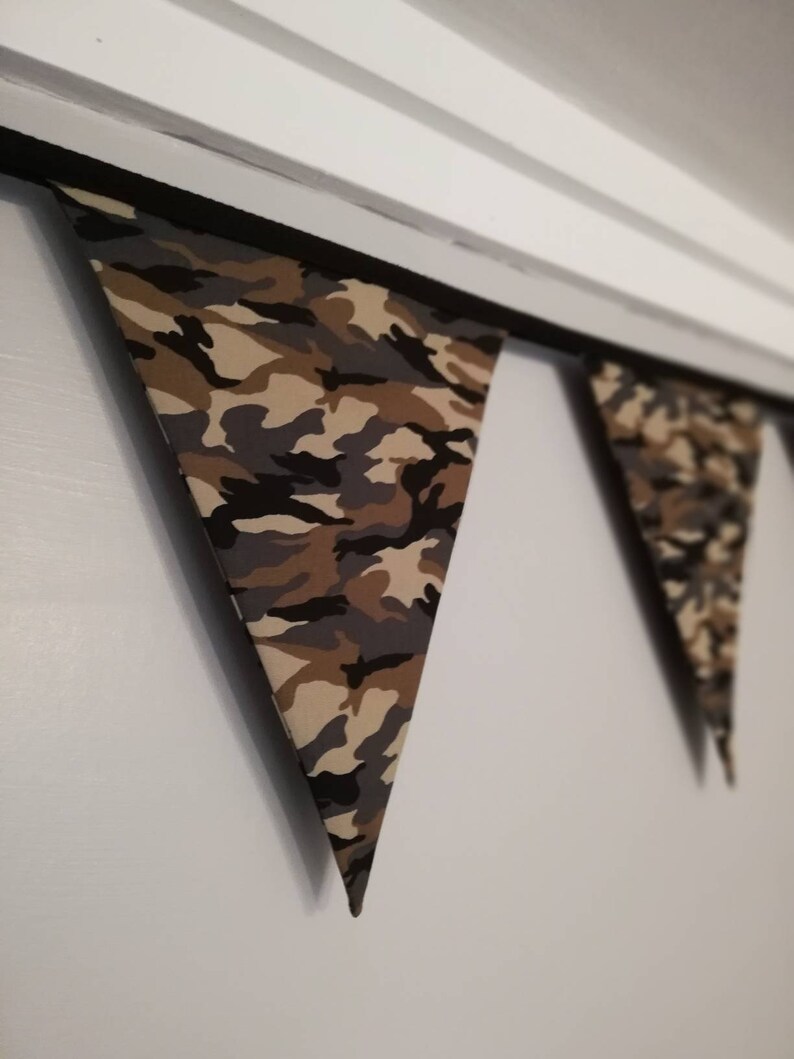 Puede incluir: Una guirnalda de tela con estampado de camuflaje con banderas triangulares que cuelgan de una cuerda negra.