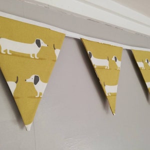 May include: A yellow and white bunting with a dachshund pattern. The bunting is made of fabric and has a white trim.