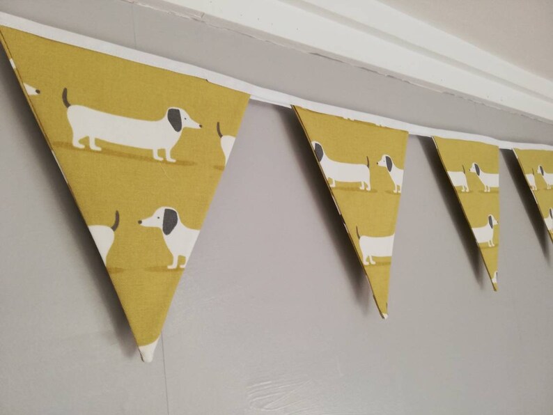 May include: A yellow and white bunting with a dachshund pattern. The bunting is made of fabric and has a white trim.