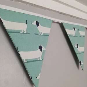 May include: A green and white bunting with a repeating pattern of dachshunds. The bunting is hung from a white ceiling.