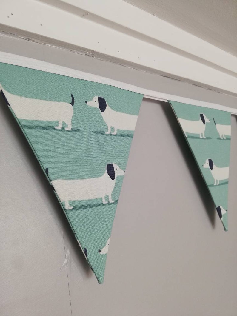 May include: A green and white bunting with a repeating pattern of dachshunds. The bunting is hung from a white ceiling.