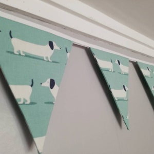 May include: A teal blue and white bunting with a repeating pattern of dachshund dogs. The bunting is strung up on a white ceiling.