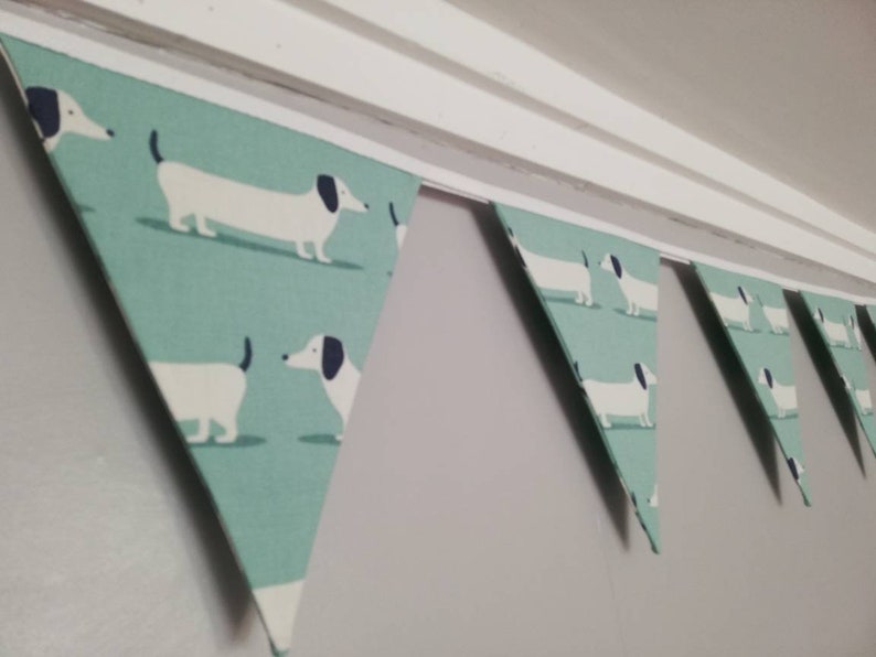 May include: A teal blue and white bunting with a repeating pattern of dachshund dogs. The bunting is strung up on a white ceiling.