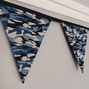 Puede incluir: Una guirnalda de banderas triangulares de tela de camuflaje azul y negro.