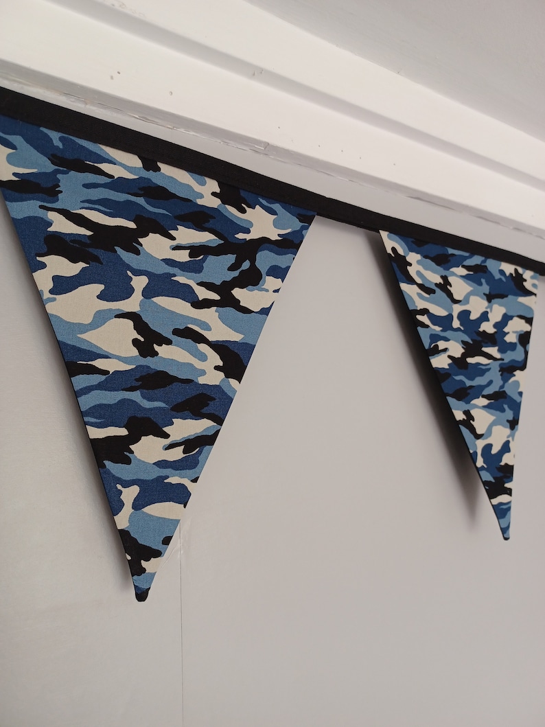 Puede incluir: Una guirnalda de banderas triangulares de tela de camuflaje azul y negro.