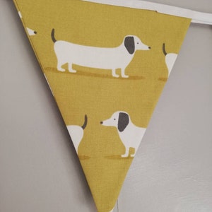 May include: A yellow triangular fabric banner with a white border and a repeating pattern of white dachshunds with black ears and noses.