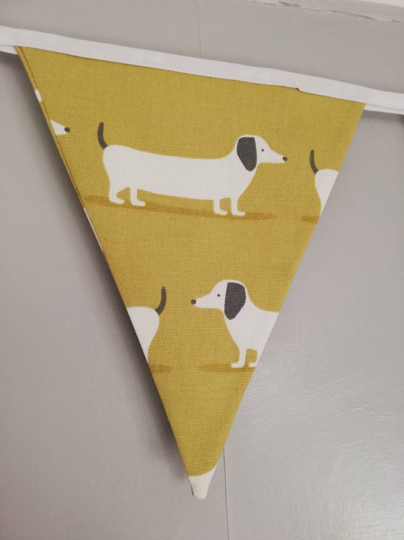 May include: A yellow triangular fabric banner with a white border and a repeating pattern of white dachshunds with black ears and noses.