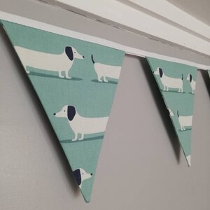 May include: A green and white bunting with a dachshund pattern. The bunting is made of fabric and has a white trim.