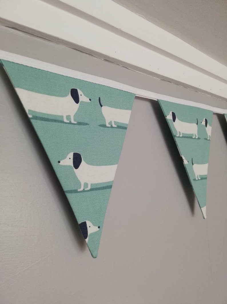 May include: A green and white bunting with a dachshund pattern. The bunting is made of fabric and has a white trim.