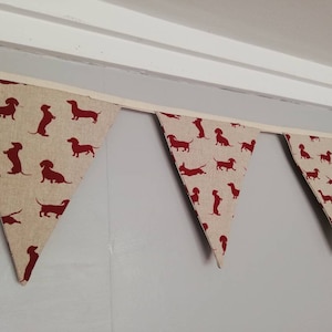 May include: A red and white bunting with a dachshund silhouette pattern. The bunting is made of fabric and is strung together with white ribbon.