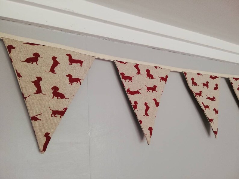 May include: A red and white bunting with a dachshund silhouette pattern. The bunting is made of fabric and is strung together with white ribbon.