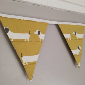 May include: A yellow and white bunting with a dachshund pattern. The bunting is made of fabric and has a white trim.