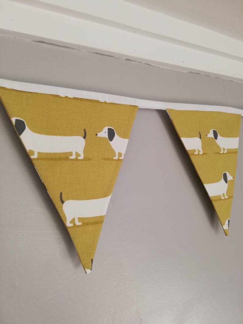 May include: A yellow and white bunting with a dachshund pattern. The bunting is made of fabric and has a white trim.