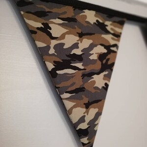Puede incluir: Una bandera triangular de tela con estampado de camuflaje y ribete negro.