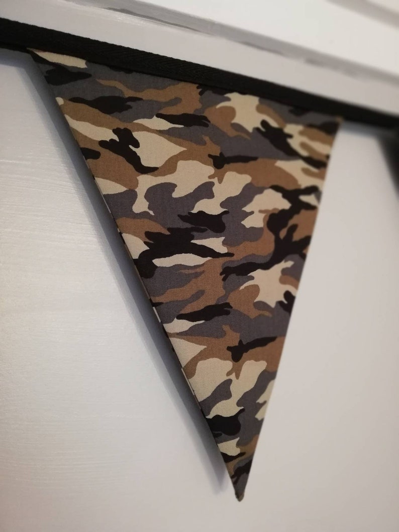 Puede incluir: Una bandera triangular de tela con estampado de camuflaje y ribete negro.