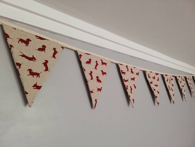 May include: A beige fabric bunting with red dachshund silhouettes. The bunting is strung up against a white ceiling.