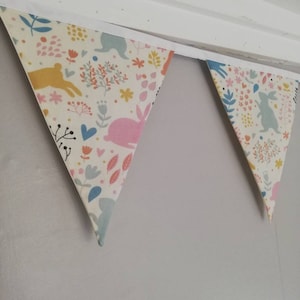 May include: A white fabric bunting with a floral and bunny pattern. The bunting is hung on a white ceiling.