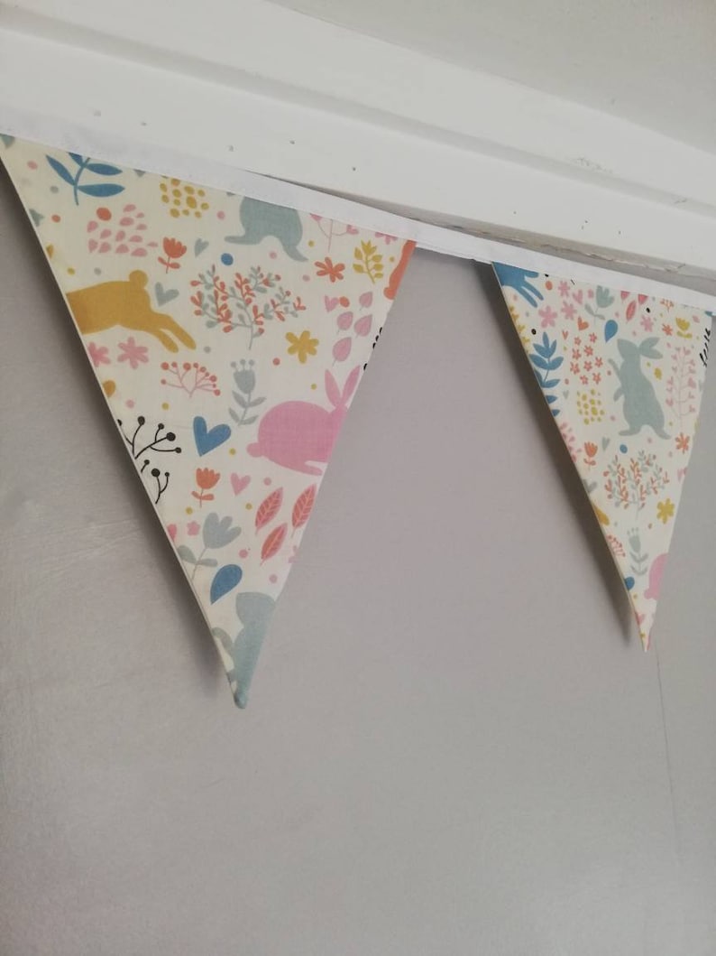 May include: A white fabric bunting with a floral and bunny pattern. The bunting is hung on a white ceiling.
