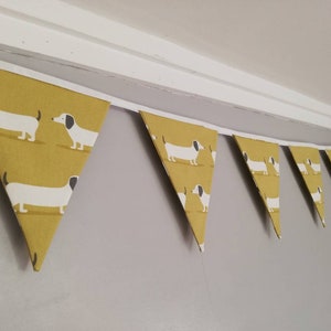 May include: A yellow and white bunting with a dachshund pattern. The bunting is made of fabric and has a white string running through it.