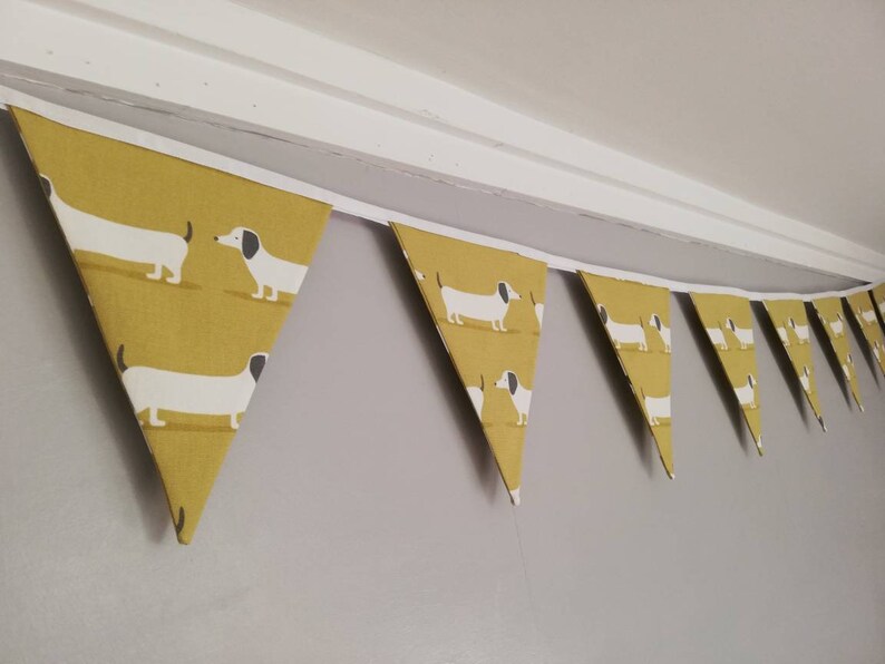 May include: A yellow and white bunting with a dachshund pattern. The bunting is made of fabric and has a white string running through it.