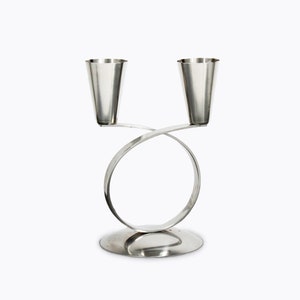 Peut inclure: Un chandelier en argent avec deux bougeoirs. Les bougeoirs sont fixés à une base circulaire incurvée.