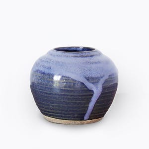 May include: A small, round ceramic vase with a blue and purple glaze. The glaze has a drip effect, creating a unique and artistic look.