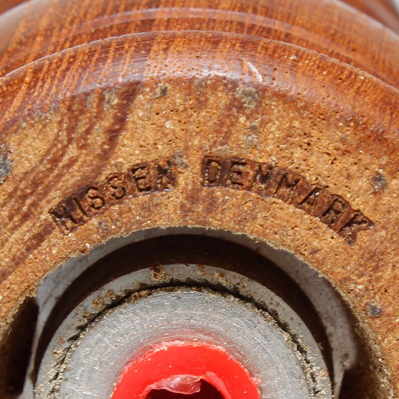 May include: Close-up of a wooden pepper mill with a metal grinder. The bottom of the mill is stamped with the words "Missen Denmark".