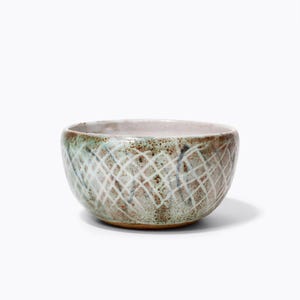 May include: A small, white ceramic bowl with a green glaze and a brown, white and grey geometric pattern.