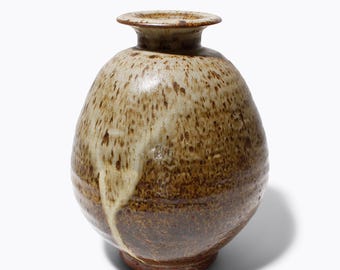 Könnte beinhalten: Eine handgefertigte Keramikvase mit rundem Körper und schmalem Hals. Die Vase hat eine gesprenkelte, erdige Farbpalette aus Braun und Creme mit einem tropfenartigen Glanzeffekt. Der Sockel ist in einem dunkleren Braunton gehalten.