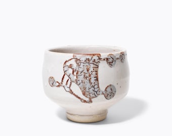 Könnte beinhalten: Eine weiße Teetasse aus Keramik mit braunem Glasurmuster. Die Tasse hat eine abgerundete Form und einen kleinen Fuß.