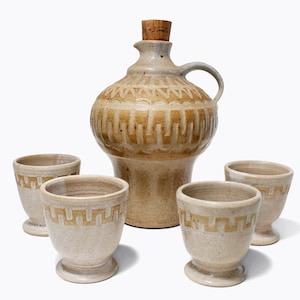 May include: A set of four ceramic cups and a ceramic jug with a cork stopper. The cups and jug are decorated with a geometric pattern in shades of brown and beige.