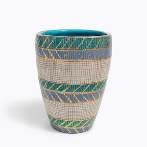 Peut inclure: Un vase décoratif en céramique avec un intérieur turquoise et un extérieur à motifs. L'extérieur présente des bandes de turquoise, de bleu et de gris avec des accents dorés. Le vase a une forme cylindrique et convient à la décoration intérieure.
