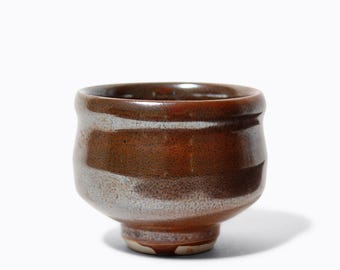 Könnte beinhalten: Eine braune Teetasse aus Keramik mit weißem Überzug. Die Tasse hat eine abgerundete Form und einen kleinen Fuß.