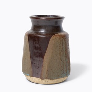 May include: A handcrafted ceramic vase with a dark brown rim and a body featuring a geometric design in shades of brown, tan, and teal. The vase has a textured surface and a beige base, perfect for home decor.