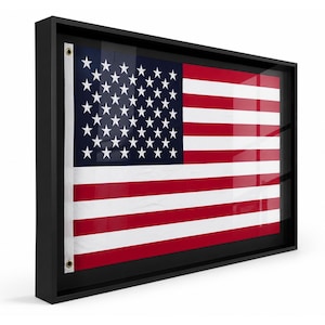 May include: Framed American flag with a black border. The flag features red and white stripes and a blue canton with white stars. The flag is displayed in a black frame with a glass cover.