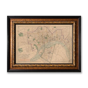 May include: A framed historical map of the cities of Richmond and Manchester, Virginia, featuring detailed street layouts, a winding river, and green park areas. The map is enclosed in a dark brown and gold ornate wooden frame with carved details.