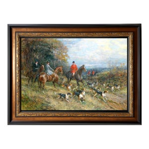 Op de afbeelding: Een antiek ingelijst schilderij toont een vossenjachtscène. Ruiters te paard in formele kleding worden vergezeld door een roedel honden. Het kunstwerk toont een landschap met bomen, velden en een bewolkte lucht, omlijst in een decoratieve goud- en zwarte lijst.